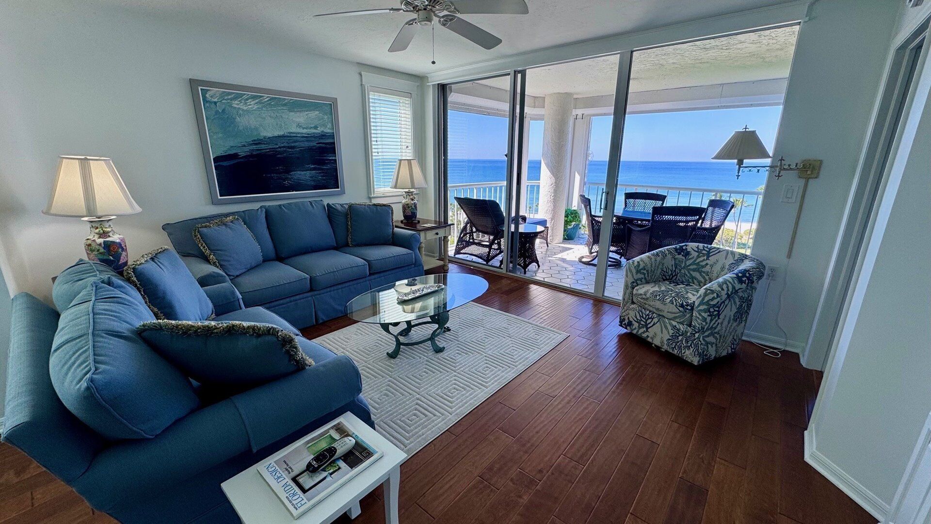 A living room with a blue sofa, a coffee table, and a view of the ocean through large glass doors.