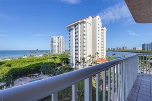 A high-rise building with a view of the ocean and a landscaped area with palm trees. - Bright open 2 bedroom beachfront condo - CL0403 (Naples)