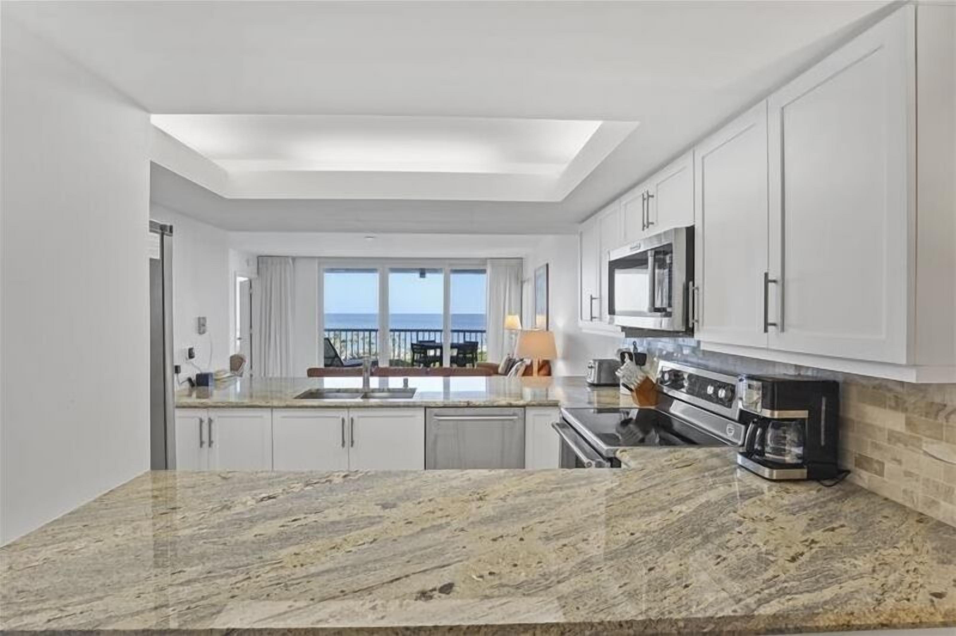 A modern kitchen with a large island, white cabinetry, and a view to the outside.