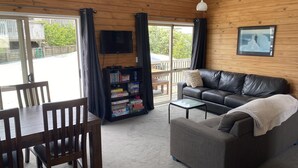 Uma sala de estar acolhedora com um sofá de couro, uma mesa de centro e uma estante repleta de livros e jogos.