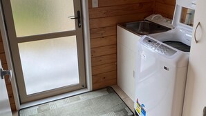 Cozinha pequena e compacta com paredes de madeira, uma pia de aço inoxidável e uma máquina de lavar branca.