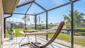 A hammock on a balcony with a view of palm trees and a body of water. - Beauty, Tranquility & Harmony. Water Views, Heated Pool  - Villa Paradise - Roelens Vacations (Cape Coral)