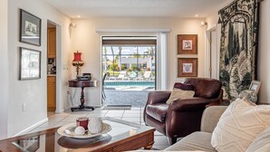 A living room with a leather sofa, a glass coffee table, and a view of a pool and outdoor area. - Beauty, Tranquility & Harmony. Water Views, Heated Pool  - Villa Paradise - Roelens Vacations (Cape Coral)