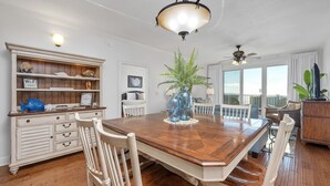 Een eetgedeelte met een houten tafel, witte stoelen, een decoratieve vaas en een witte kast met planken.