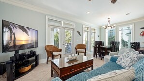 Una sala de estar con televisor, sillas de mimbre, un sofá y un comedor con mesa y sillas.