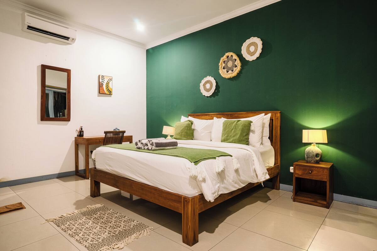 A bedroom with a wooden bed, green wall decor, a bedside table with a lamp, and a small rug.