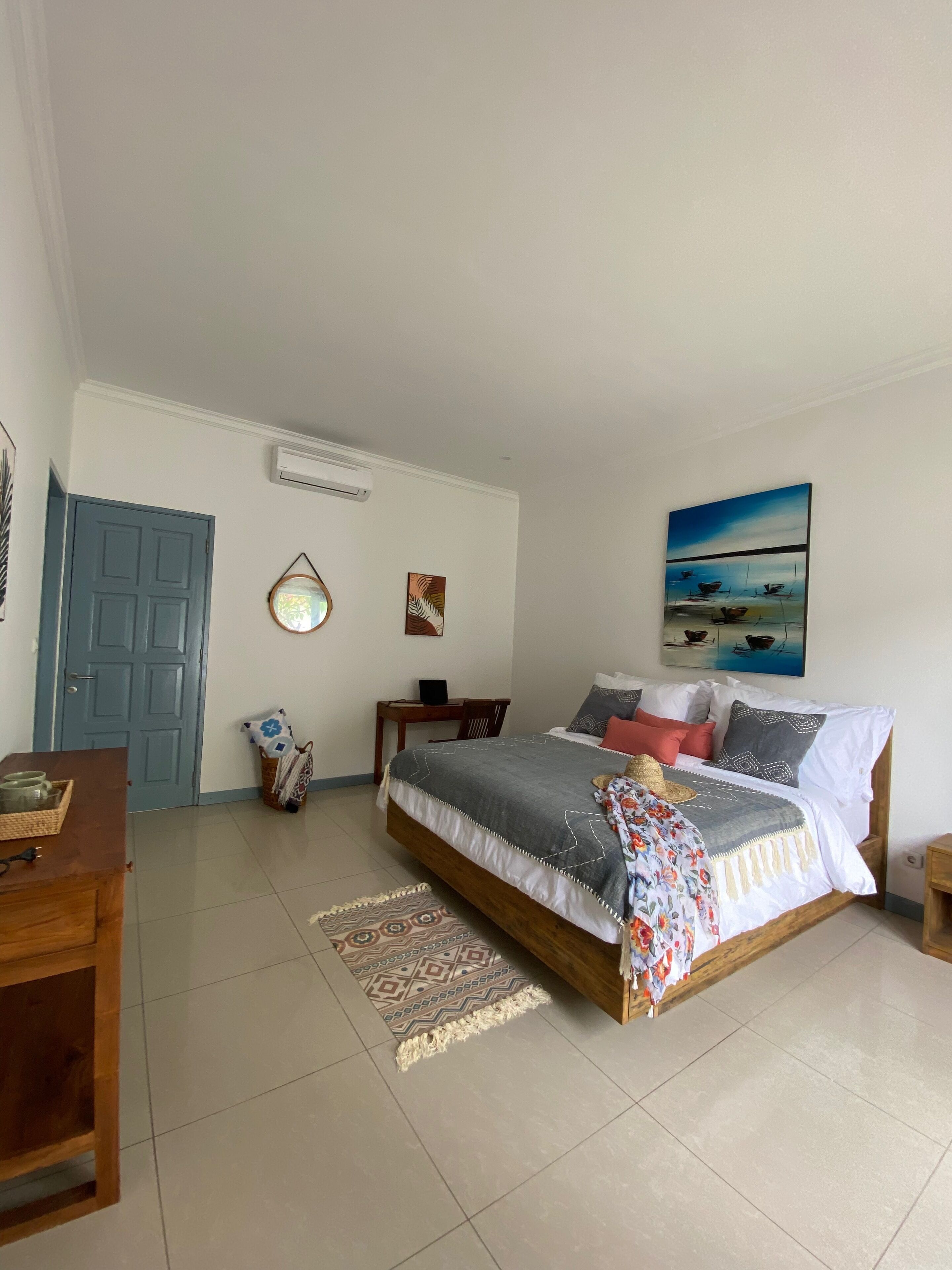 A bedroom with a bed, a desk, a chair, a door, and a painting on the wall.