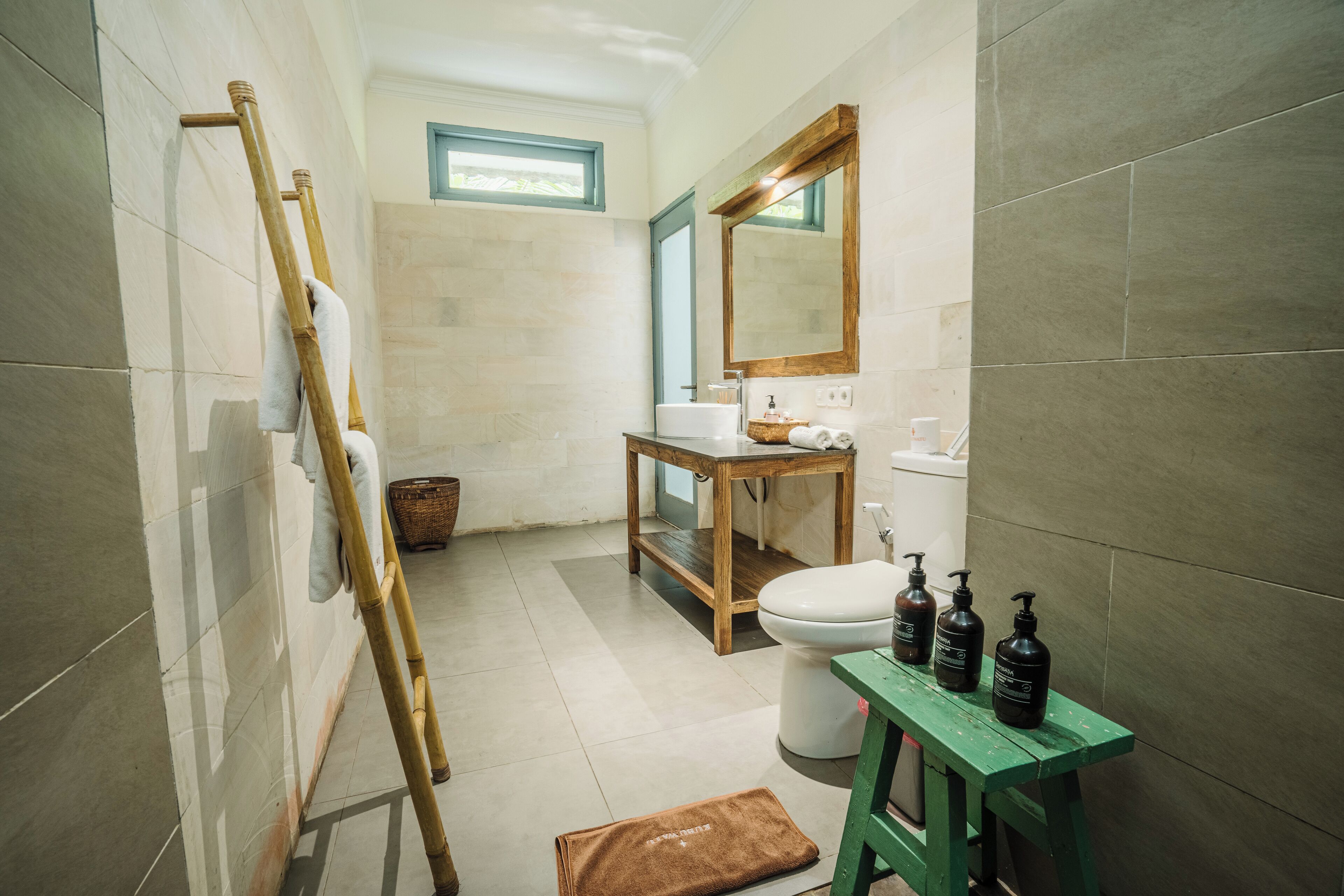 Un baño con tocador de madera, inodoro y un taburete verde.