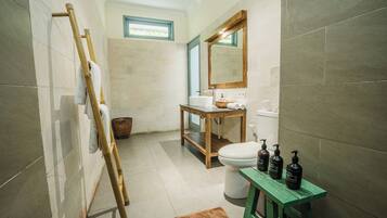 Un baño con tocador de madera, inodoro y un taburete verde.