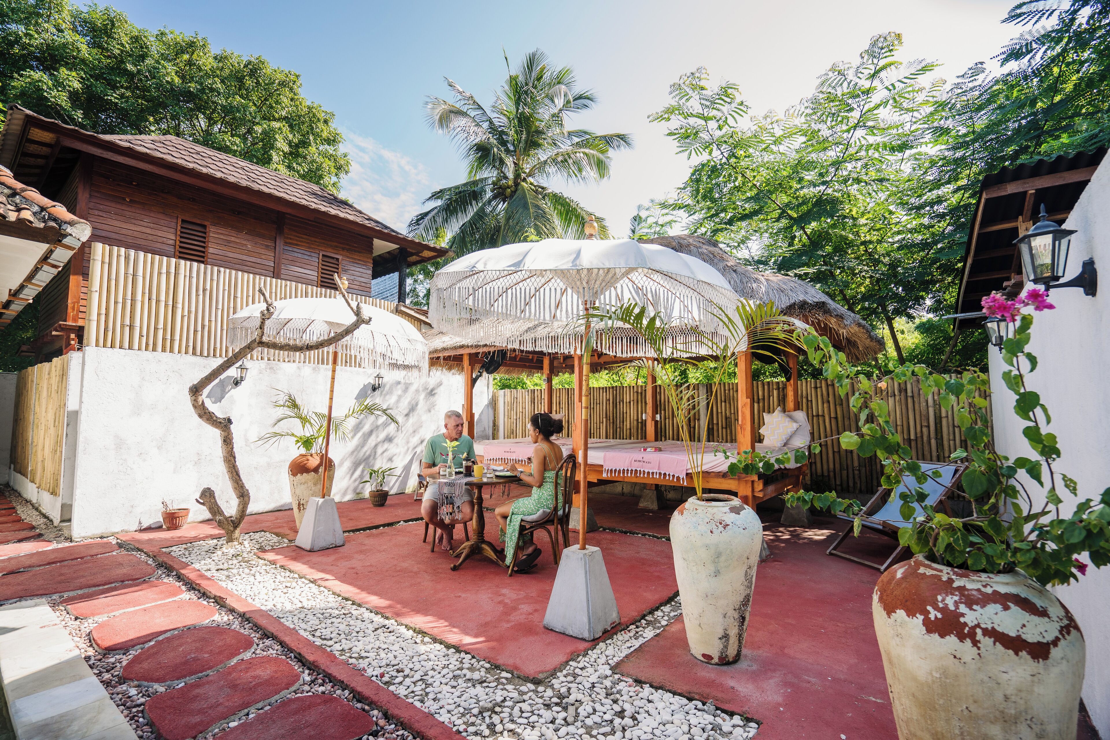A patio with a table and chairs, surrounded by potted plants and a large decorative vase.