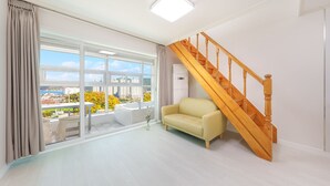 Amplia habitación con un gran ventanal con vista a la ciudad, una escalera de madera y un sofá color beige.