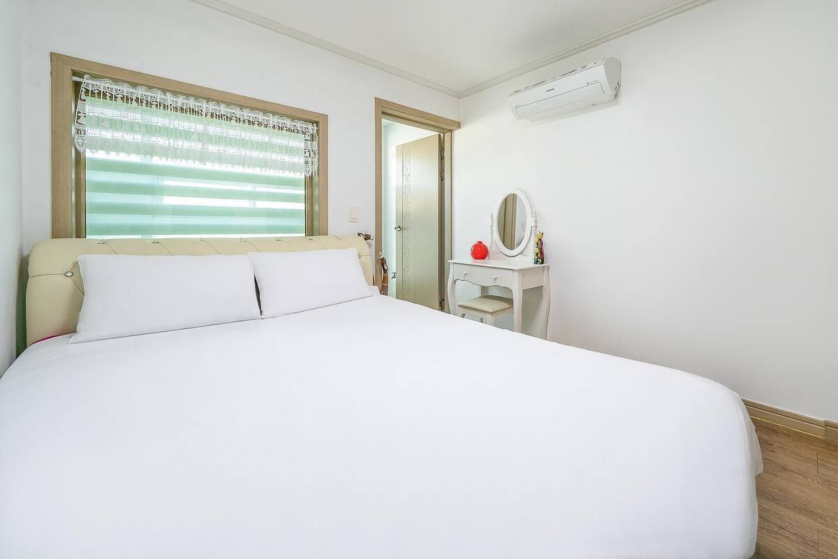 A hotel room with a bed, a vanity with a mirror, and an air conditioning unit.
