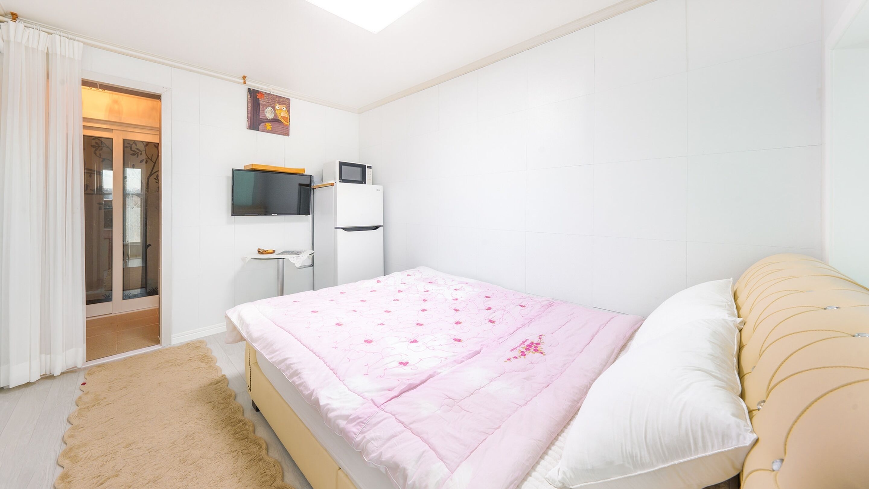A bedroom with a bed, a TV, a small table, and a window with curtains.