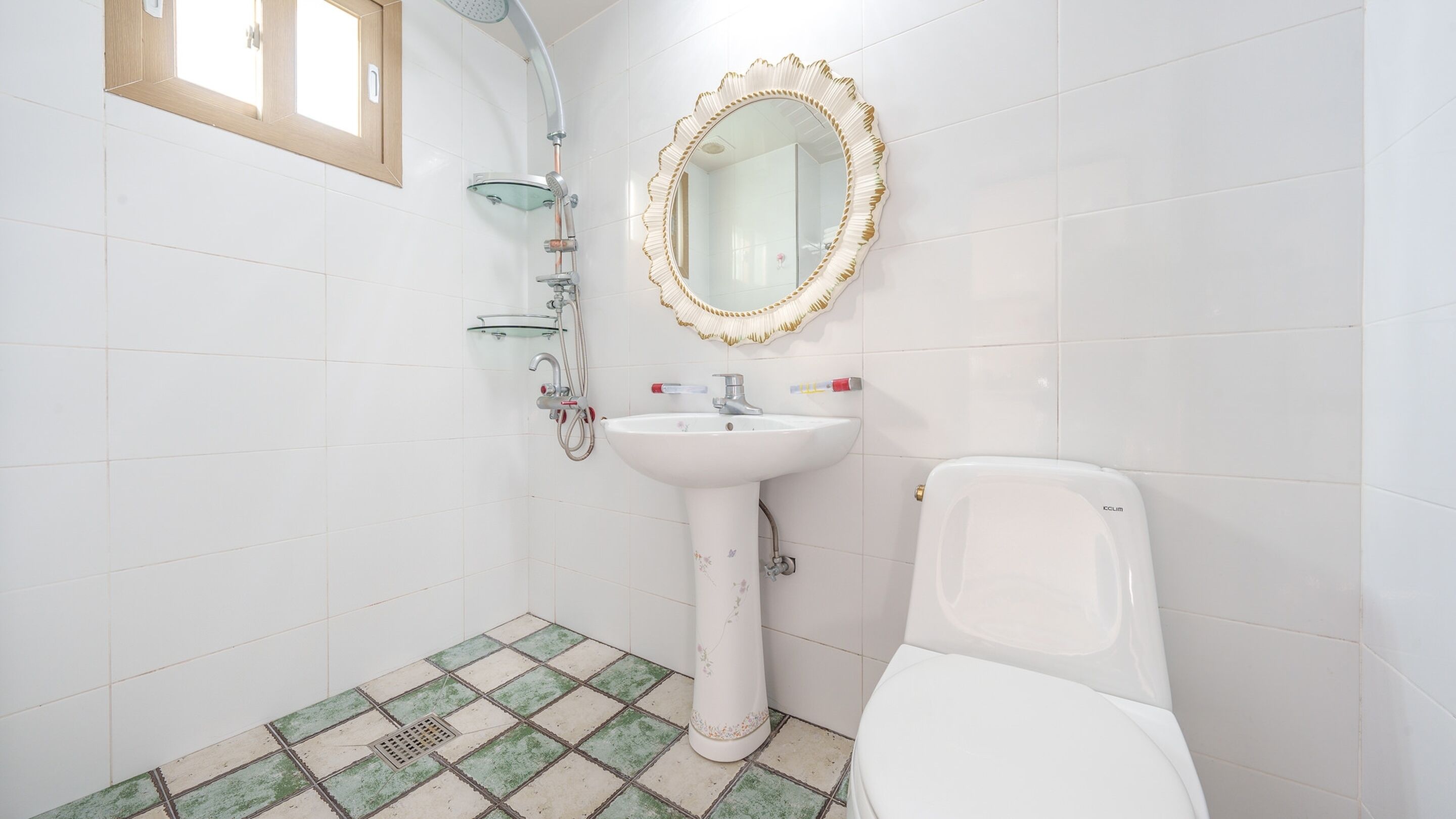 A bathroom with a white sink, a mirror with a decorative frame, a showerhead, and a toilet. The floor has a green and white checkered pattern.