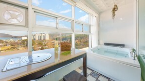 Un baño con bañera, una ventana que ofrece vistas a la ciudad y una botella de vino sobre el mostrador.
