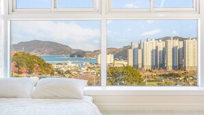 Un dormitorio con un gran ventanal que da a una ciudad costera, con edificios altos y una masa de agua.