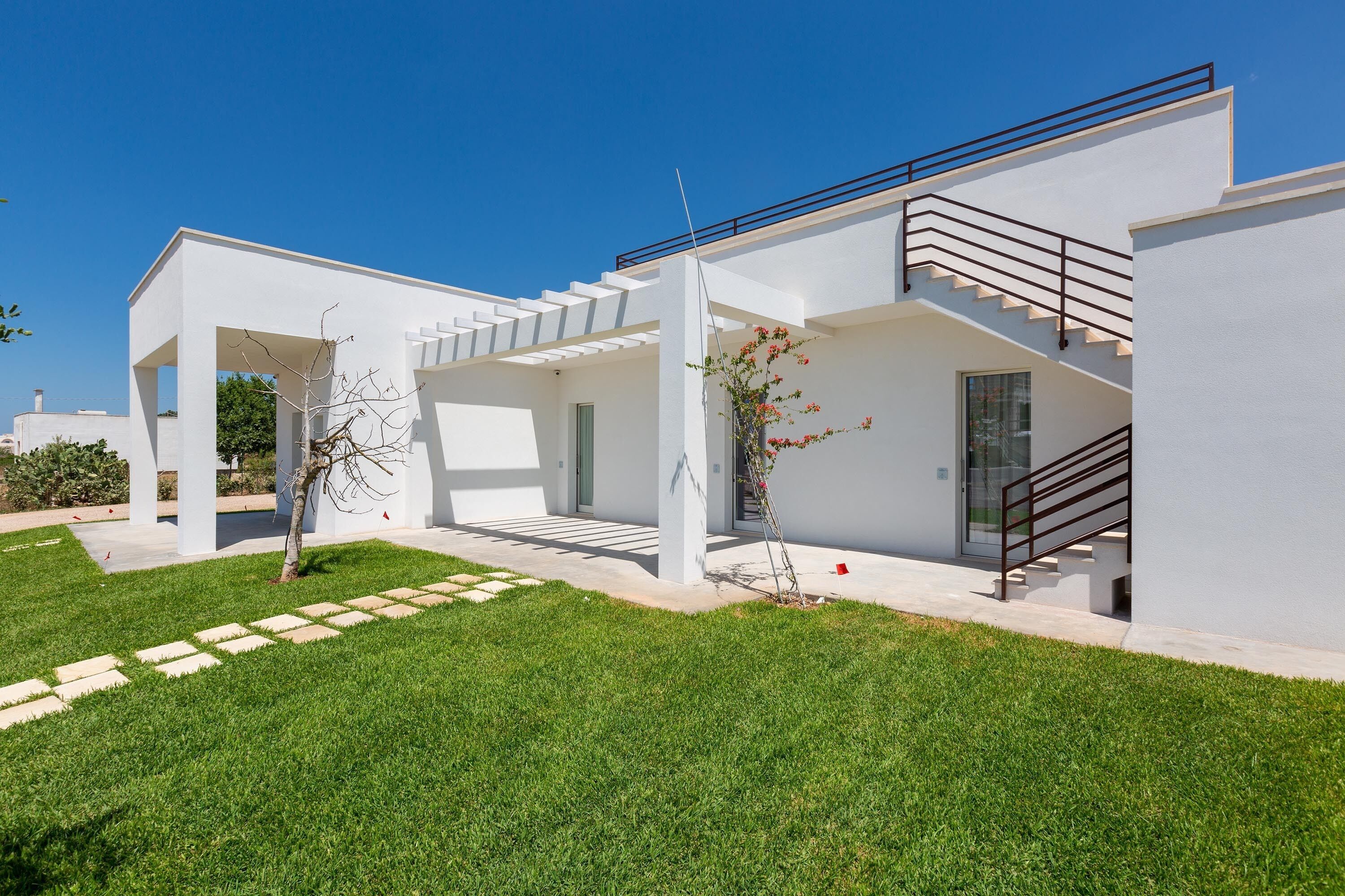A modern house with a white exterior, a covered patio area, and a staircase leading to the upper floor.