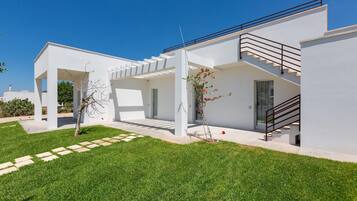 A modern house with a white exterior, a covered patio area, and a staircase leading to the upper floor.