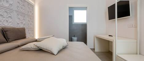 Un dormitorio moderno con cama, almohadas, televisor y armario empotrado.