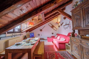 Ein gemütliches Dachzimmer mit Esstisch, gedecktem Tisch, einem roten Sofa und einem Holzschrank.