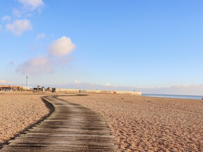 Una playa de guijarros con un paseo marítimo de madera que conduce a un muelle.