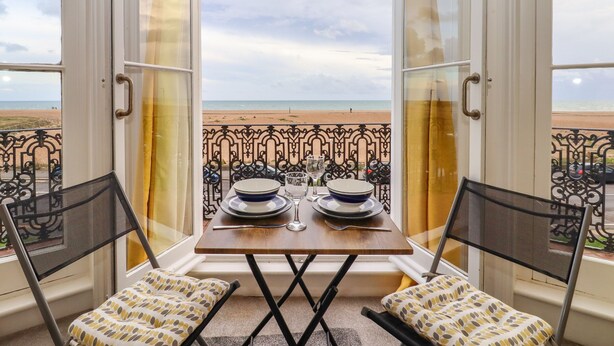 A balcony with a table set for two, overlooking a beach. - The Old Spy Headquarters (Folkestone)