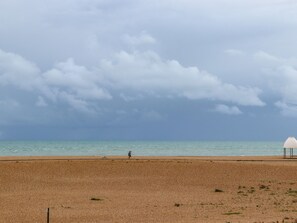 A beach with a person walking, a dog, and a white structure. - The Old Spy Headquarters (Folkestone)