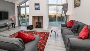 Ein modernes Wohnzimmer mit Kamin, grauen Sofas, einem roten Teppich mit Muster und großen Fenstern mit Blick ins Freie.