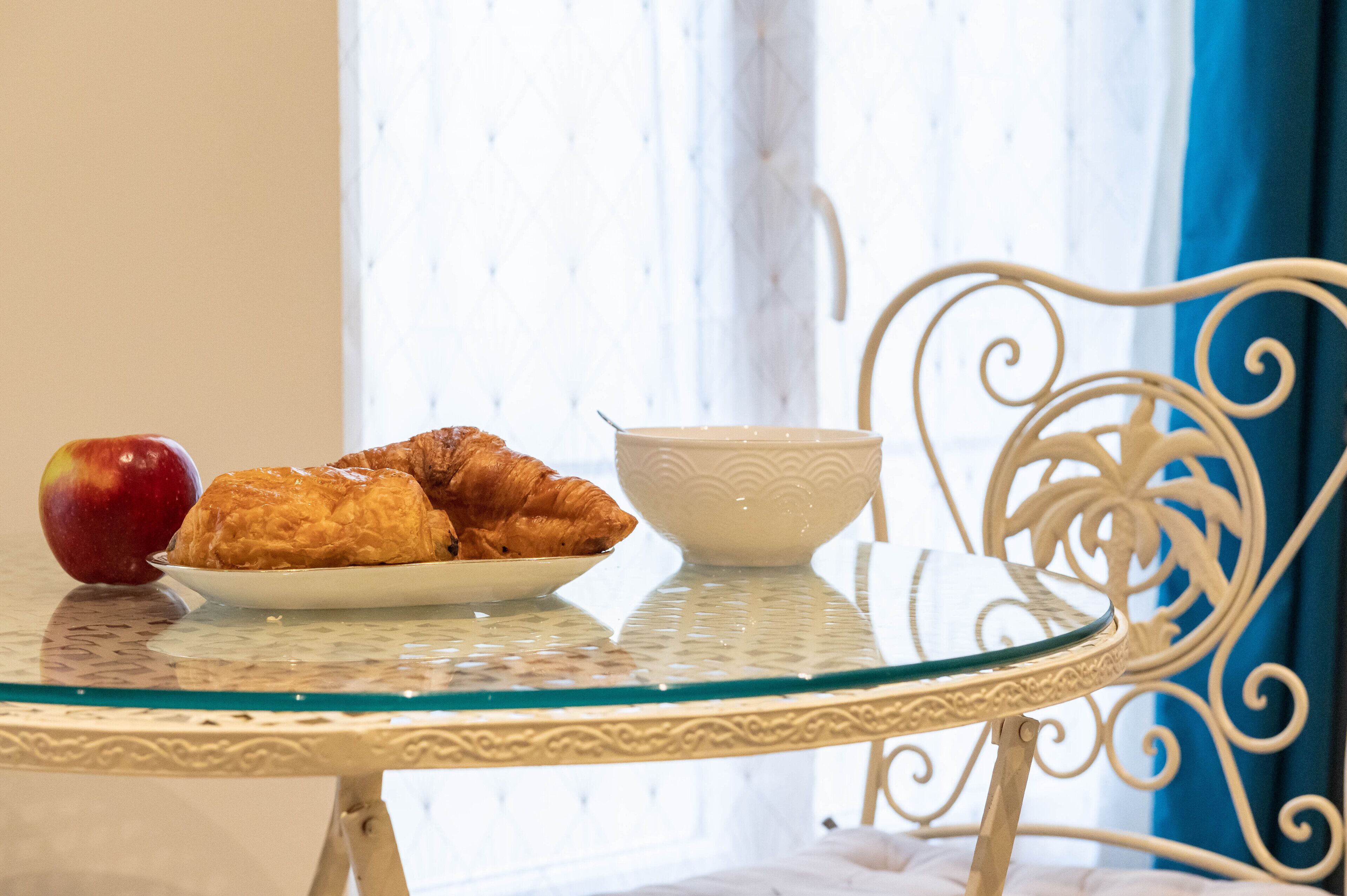 A breakfast setting with croissants, an apple, and a cup on a glass table.