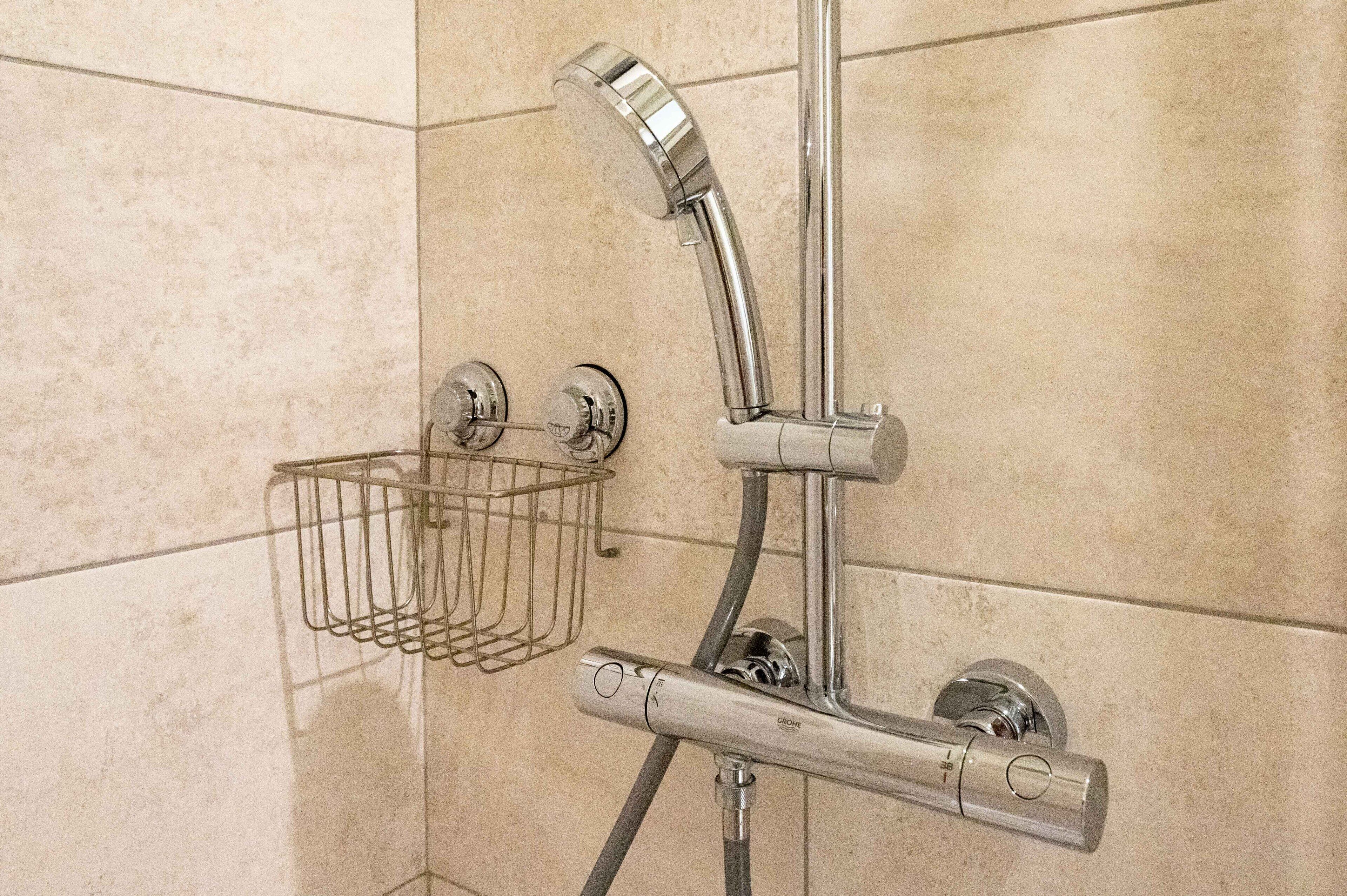 A shower with a chrome faucet and a metal showerhead, mounted on beige tiled walls.