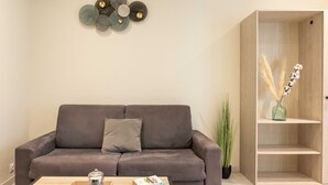 A modern living room with a grey sofa, a wooden coffee table with a book and a candle, and a decorative wall piece above the sofa.