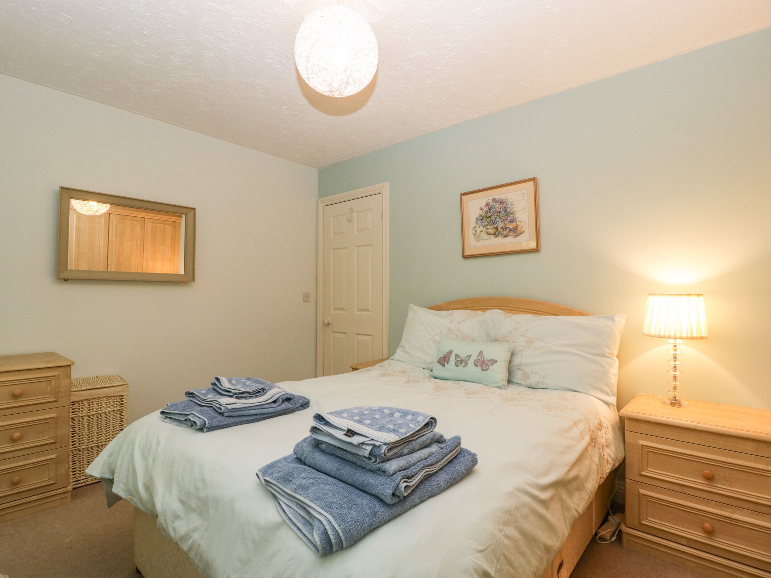A neatly made bed with folded towels, a bedside lamp, and a framed picture on the wall.
