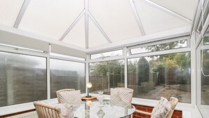 A conservatory with a glass table and wicker chairs, large windows, and a view of a garden. - 2 Bathsheba Terrace (Dorchester)