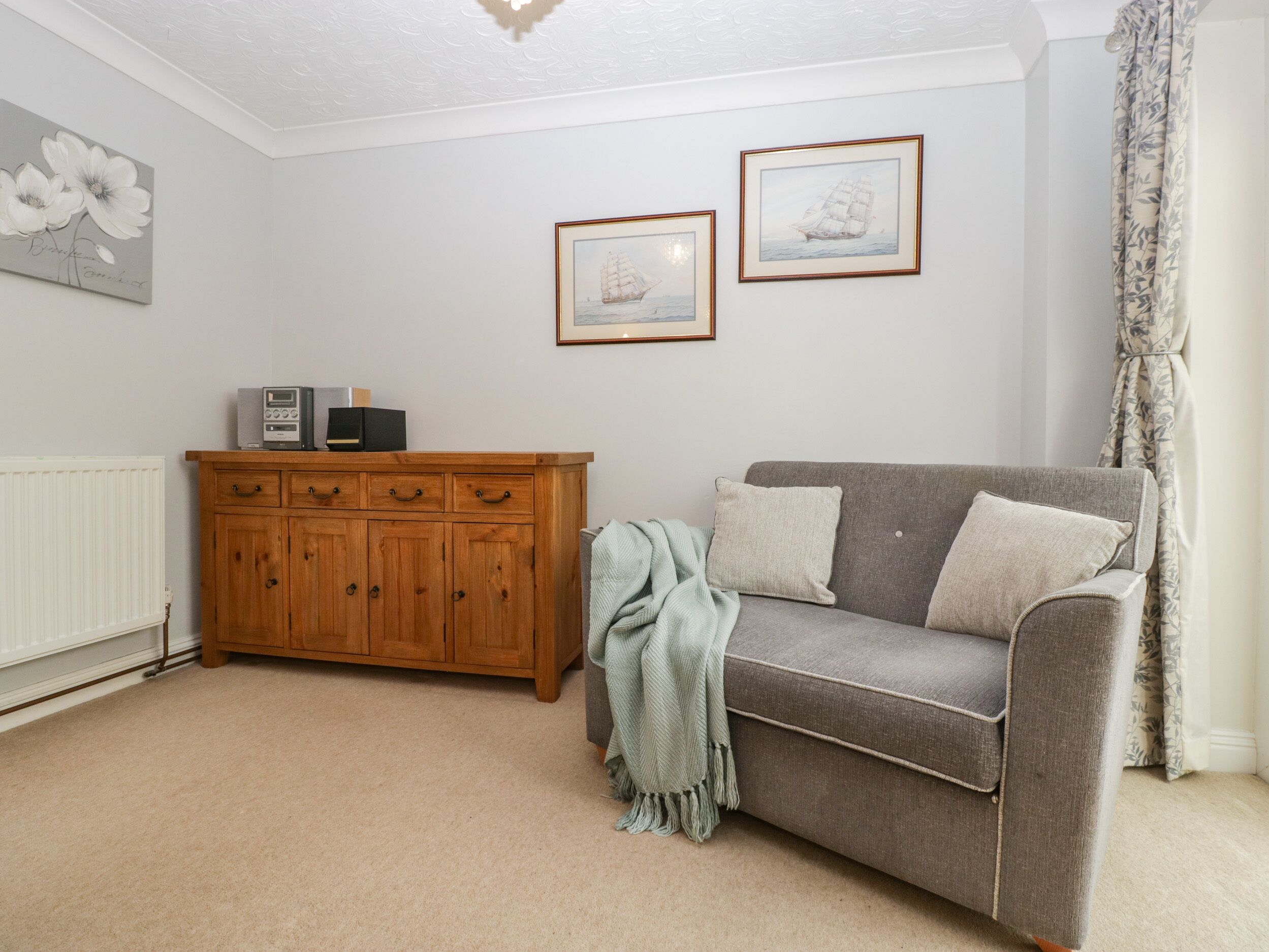 A living room with a grey sofa, a wooden cabinet, and two framed pictures on the wall.