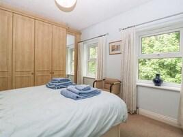 Un dormitorio con cama, una silla, un ventanal con cortinas y un armario de madera.
