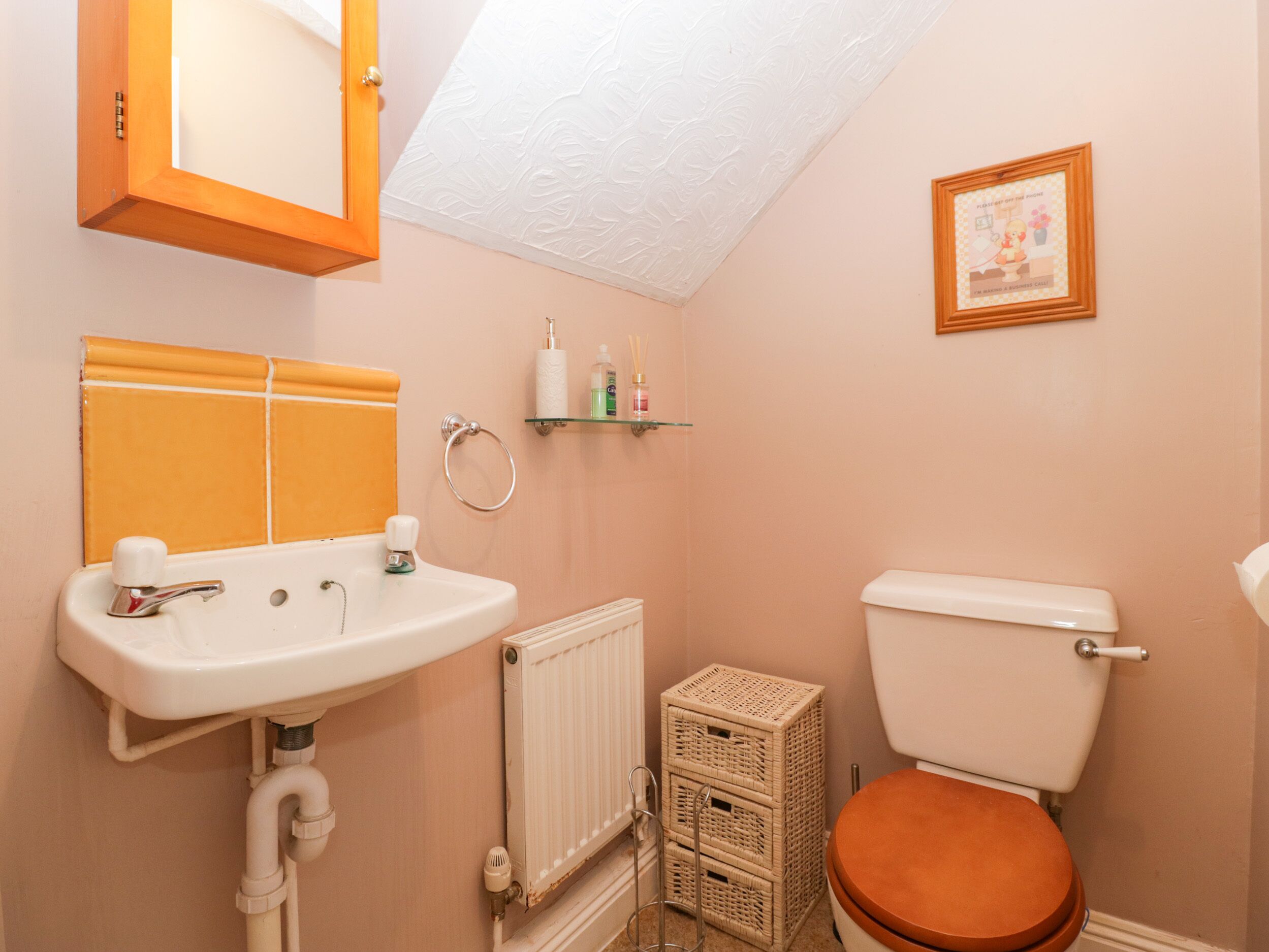 Une salle de bain avec un lavabo blanc, des toilettes, un panier en osier et un tableau encadré au mur.