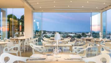 A restaurant with white chairs and tables, a glass partition, and a view of the cityscape.