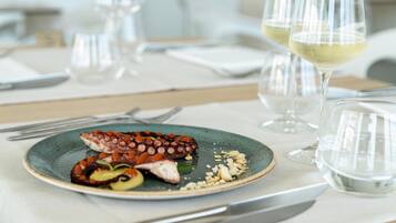 Een eettafel met een bord octopus en andere zeevruchten, twee glazen witte wijn en bestek.