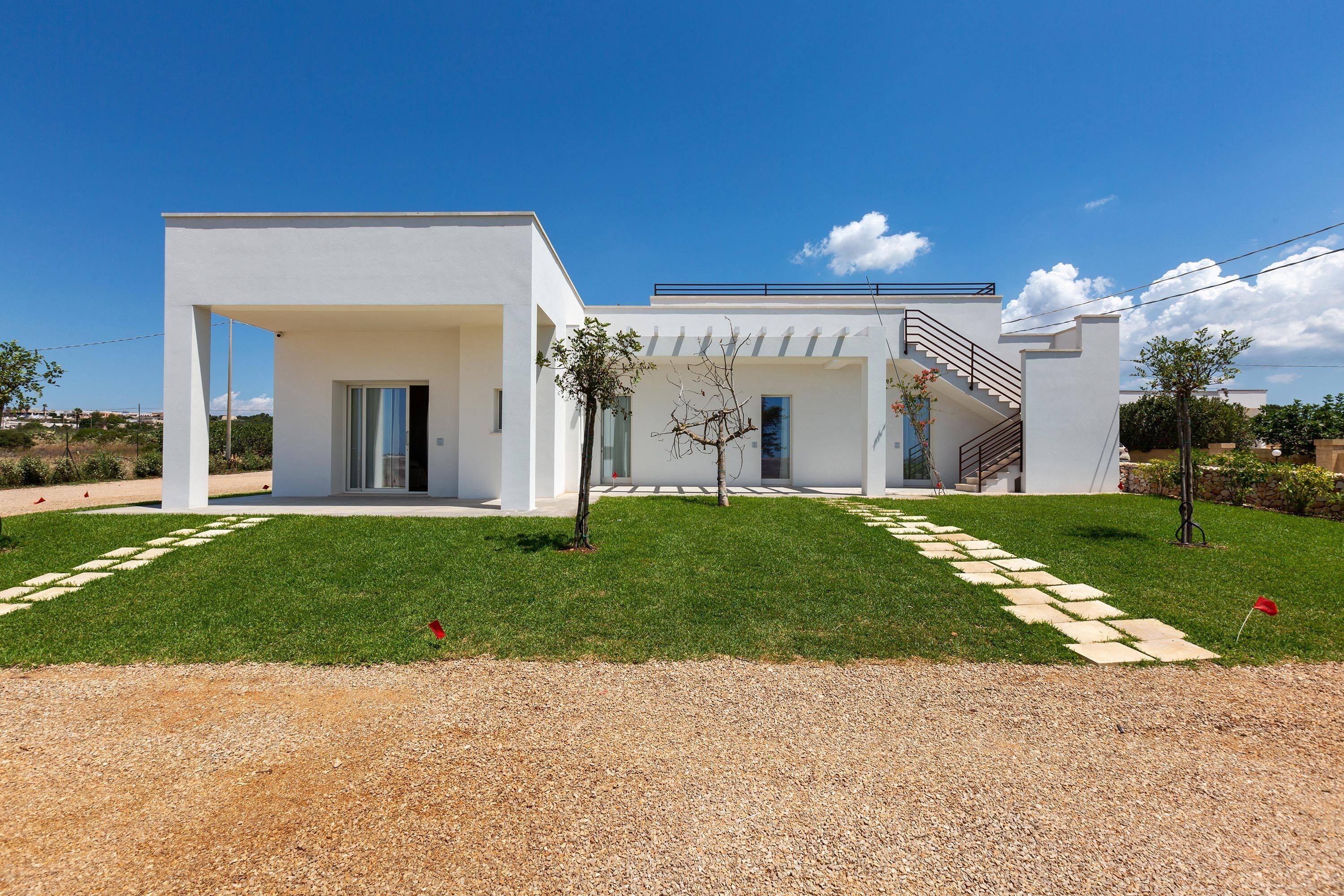 A modern house with a white exterior, a covered porch, and a staircase leading to a second floor.