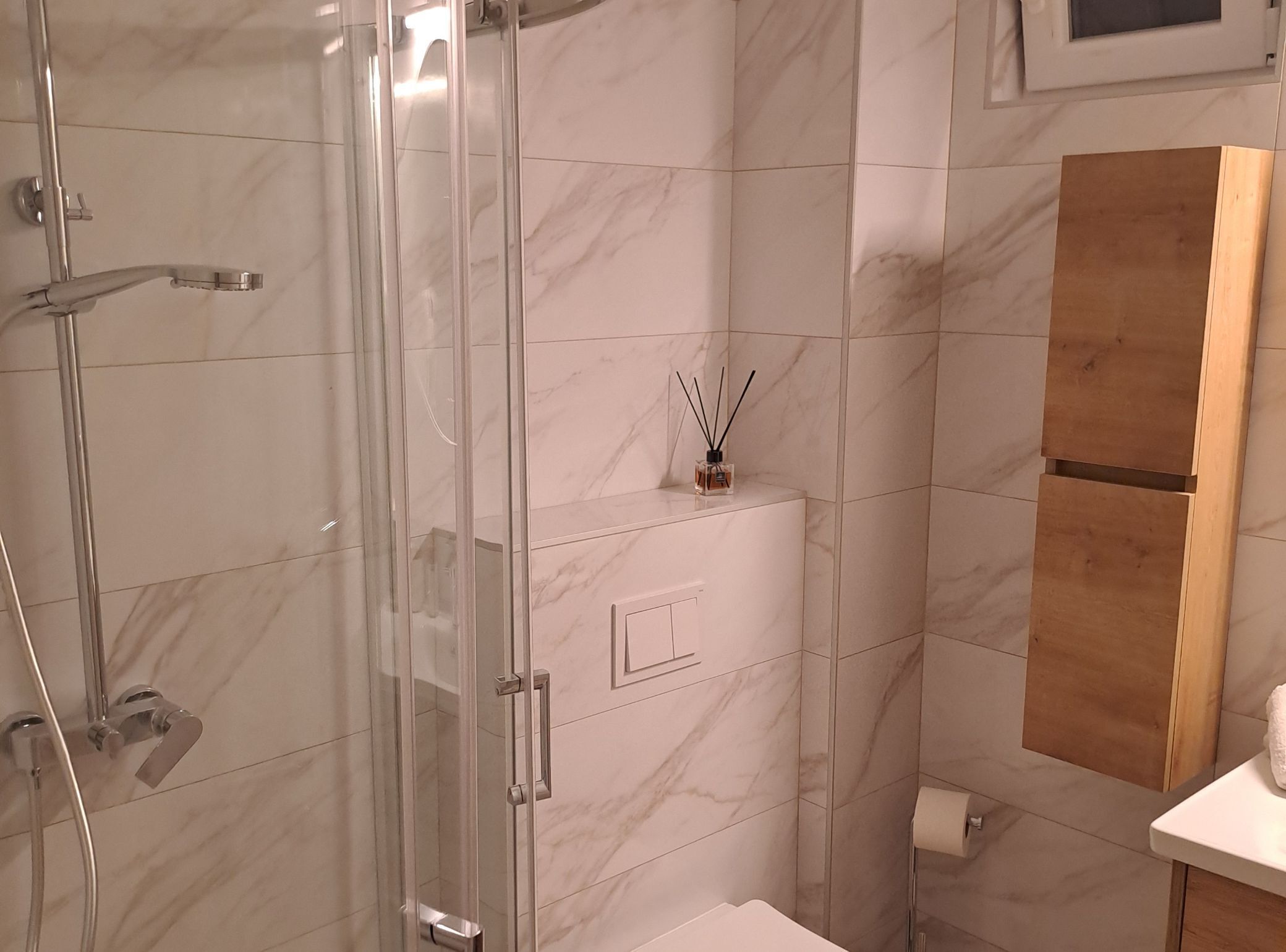 A modern bathroom with a glass shower enclosure, a toilet, and a wooden cabinet.