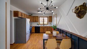 Une cuisine moderne avec des meubles en bois, un réfrigérateur en acier inoxydable, une table à manger avec des chaises et un luminaire au plafond original.