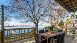 Une terrasse en bois avec une table et des chaises, offrant une vue sur une étendue d’eau et une côte lointaine.