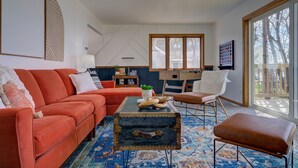 Un salon avec un canapé rouge, un fauteuil blanc, une table basse et un tapis à motifs.
