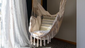 Un fauteuil suspendu en macramé avec un coussin rayé, dans une pièce dotée d’un plancher en bois et d’un mur blanc.