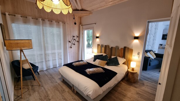 A bedroom with a large bed, bedside lamps, a standing lamp, and a view of the outdoors. - Very bright Scandinavian chalet located 3 min. from the lake and 10 min. of the (BISCARROSSE)