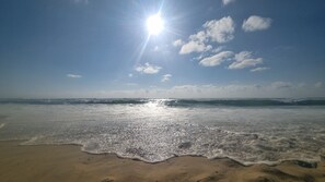 A beach with waves, a clear sky, and the sun shining.