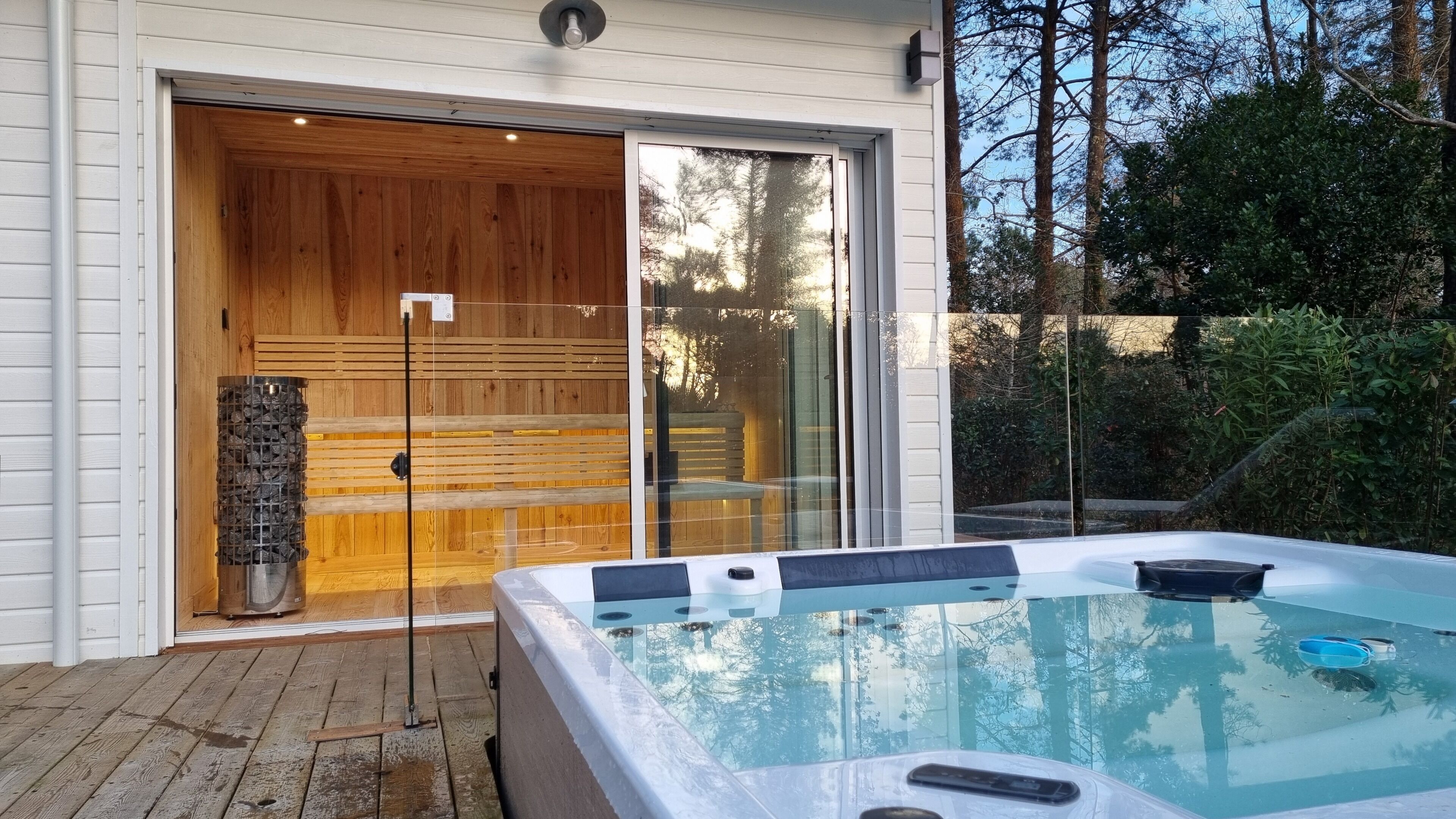 A spa area with a hot tub, wooden deck, and a glass door leading to a sauna.