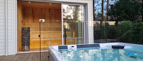 A spa area with a hot tub, wooden deck, and a glass door leading to a sauna.