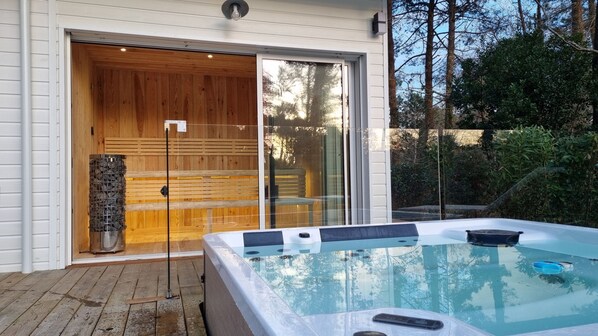 A spa area with a hot tub, wooden deck, and a glass door leading to a sauna.