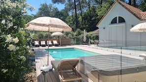 Une piscine entourĂ©e de verdure et dotĂ©e dâune terrasse en bois, avec des chaises longues et des parasols.